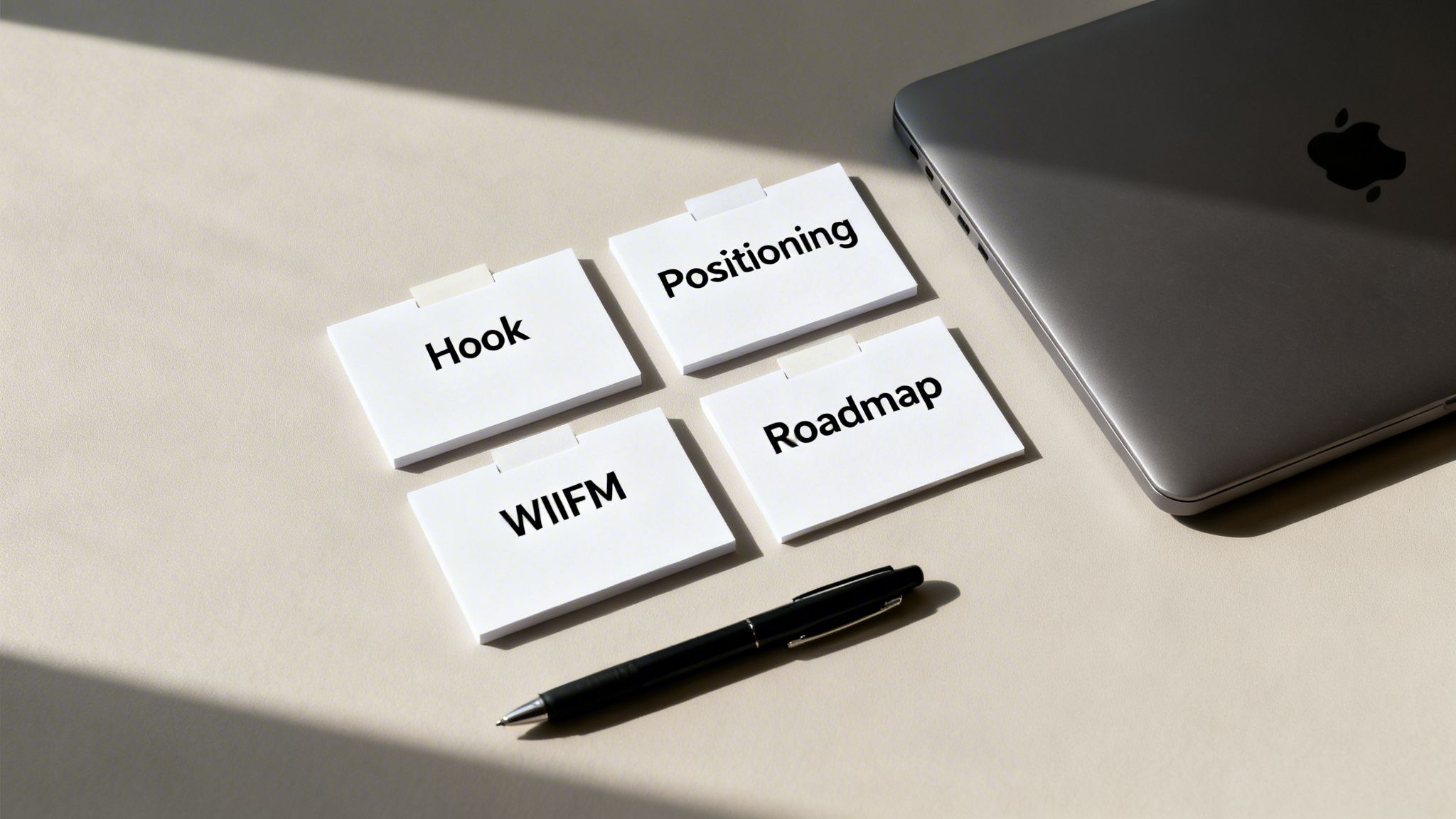 Close-up of 'Hook', 'Positioning', 'WIIFM', 'Roadmap' cards, a pen, and a laptop on a table.
