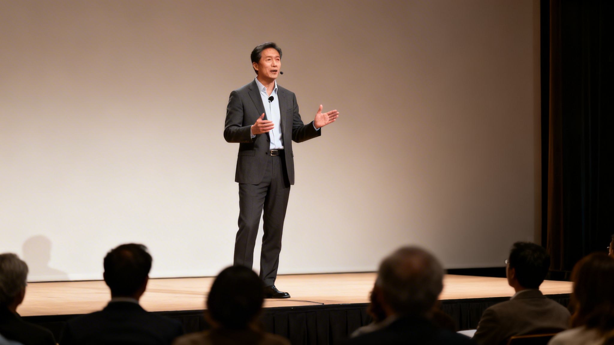 A man in a suit gives a presentation on stage, gesturing to an unseen audience.