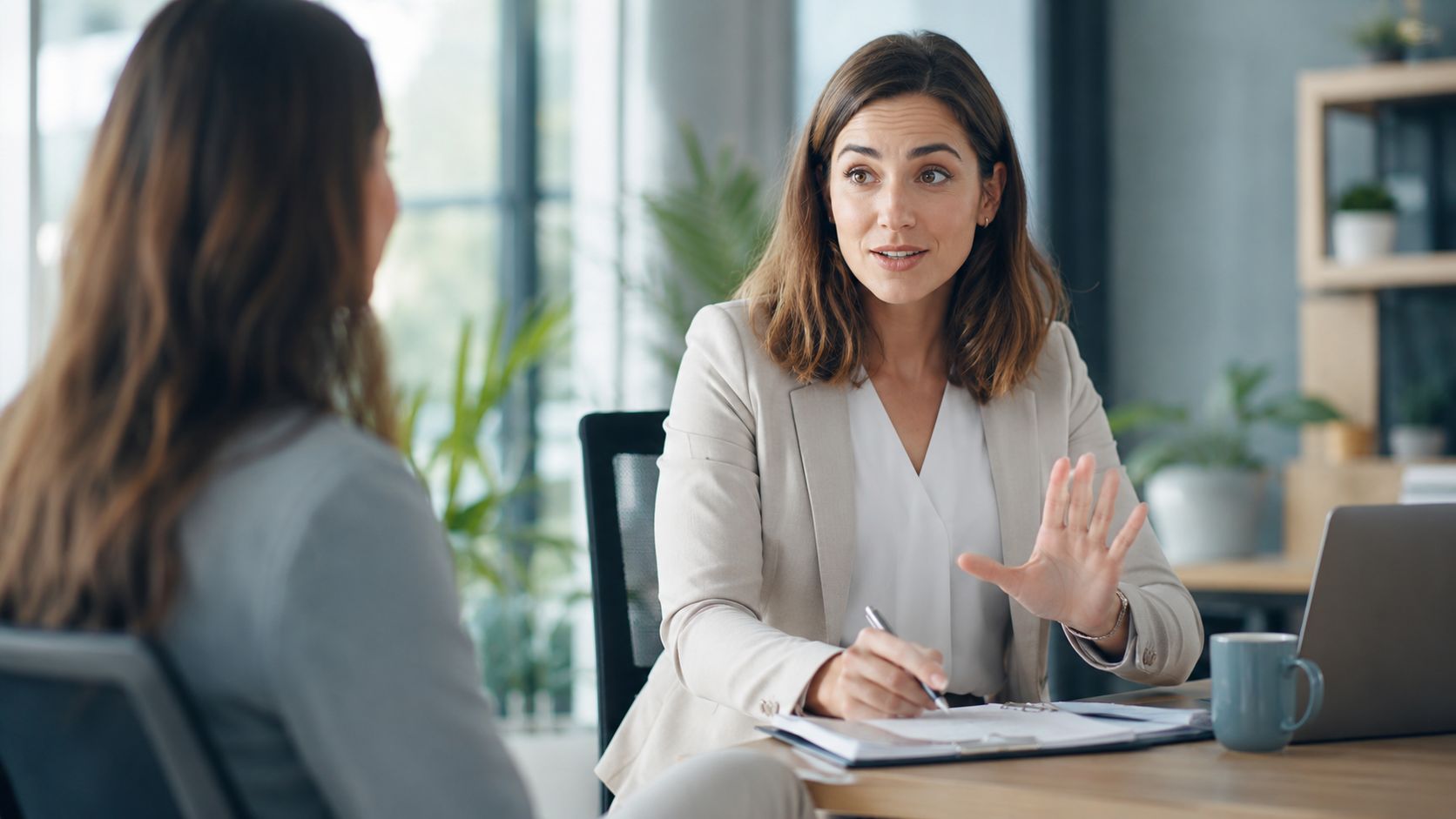 A professional woman in a suit conducting an interview with another person in an office setting.